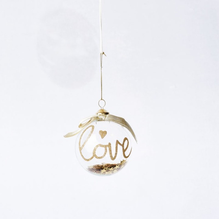 Transparante kerstbal met gouden 'love' tekst en een strikje, hangend aan een dunne draad.