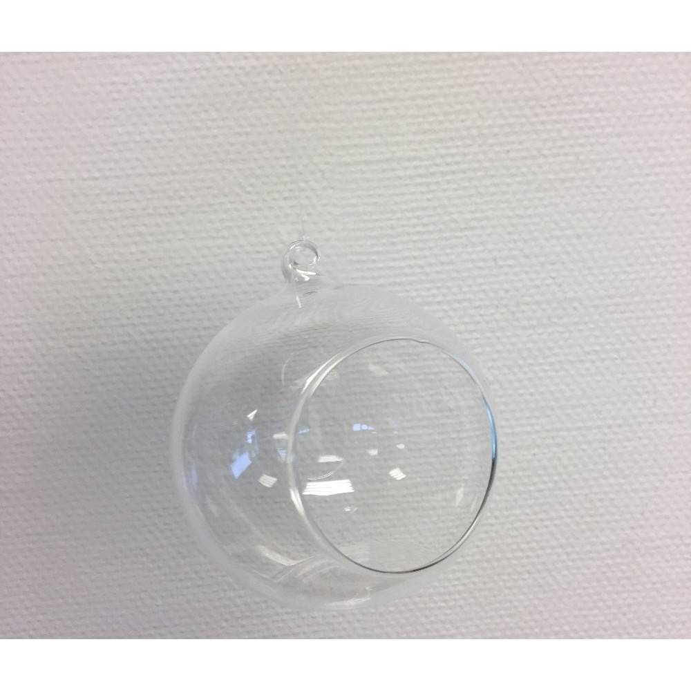 A clear glass orb with a small opening, suspended against a textured white background.