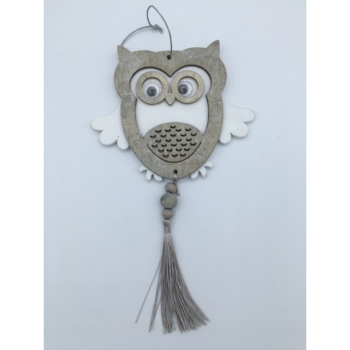 A wooden owl ornament with large eyes, white wings, and a decorative tassel below.