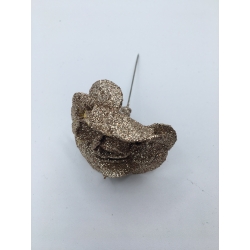 A glittery, gold-toned sculpture resembling a whimsical face with a metallic pin.