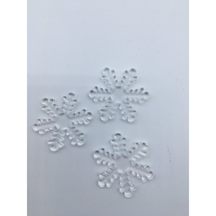 Drie doorzichtige sneeuwvlokken van kunststof liggen op een witte ondergrond.