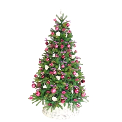 A lush green Christmas tree adorned with pink and purple ornaments in a white basket.