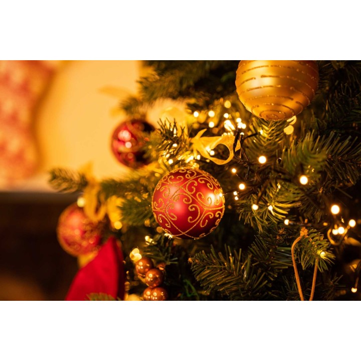 Kerstboom versierd met rode en gouden ballen, glinsterende lichtjes en groene takken.