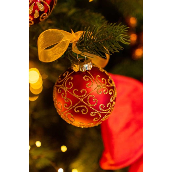 Een glanzende rode kerstbal met gouden versieringen, hangend aan een dennenboom.
