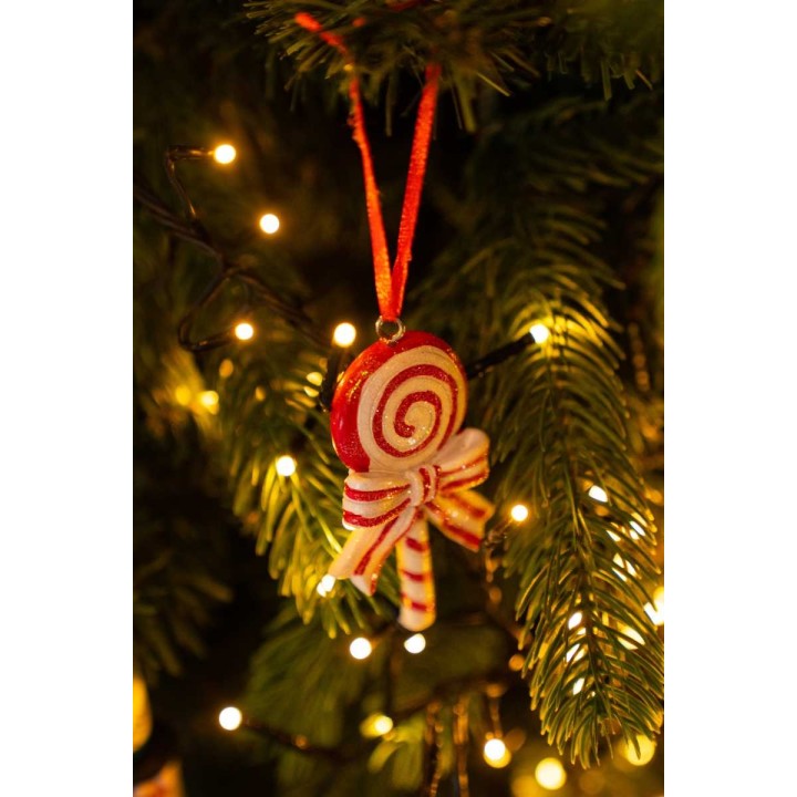 Kerstversiering in de vorm van een kleurrijke lolly, hangend aan een dennenboom met lichtjes.