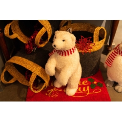 A fluffy white polar bear figurine with a red scarf beside decorative baskets on a festive mat.