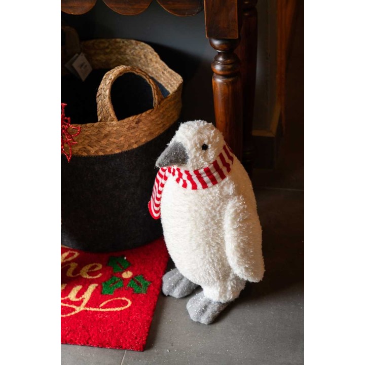 Een schattige, pluizige pinguïn met een gestreepte sjaal staat naast een mand en een vloerkleed.