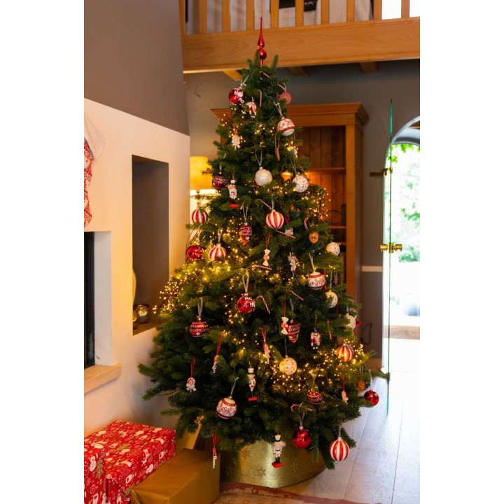 Een versierde kerstboom met rode en witte ballen, lichtjes en cadeau's eronder.