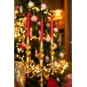 A golden candle holder with three twisted red candles in front of a decorated Christmas tree.