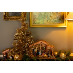 Een kersttafelstuk met een miniatuur kerststal, gouden ballen en een glinsterende boom.