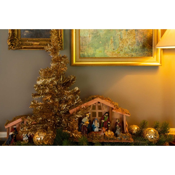 Een kersttafelstuk met een miniatuur kerststal, gouden ballen en een glinsterende boom.