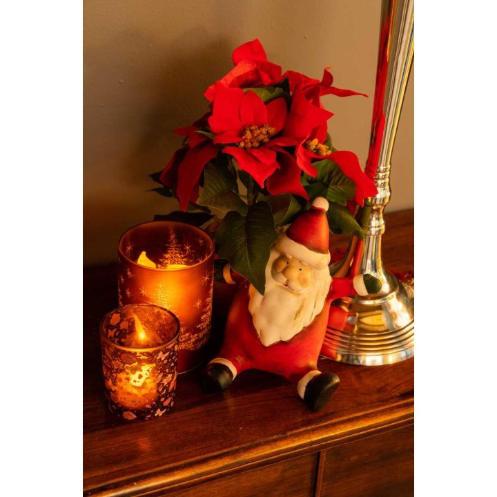 Kerstmanfiguur naast rode bloemen en sfeervolle kaarsen op een houten tafel.
