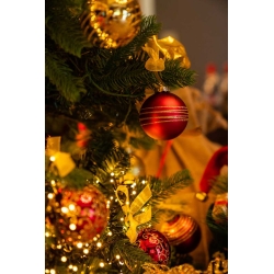 Gouden en rode kerstballen hangen tussen groene takken, omgeven door glinsterende lichtjes.