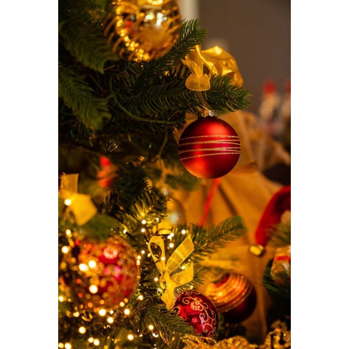 Gouden en rode kerstballen hangen tussen groene takken, omgeven door glinsterende lichtjes.