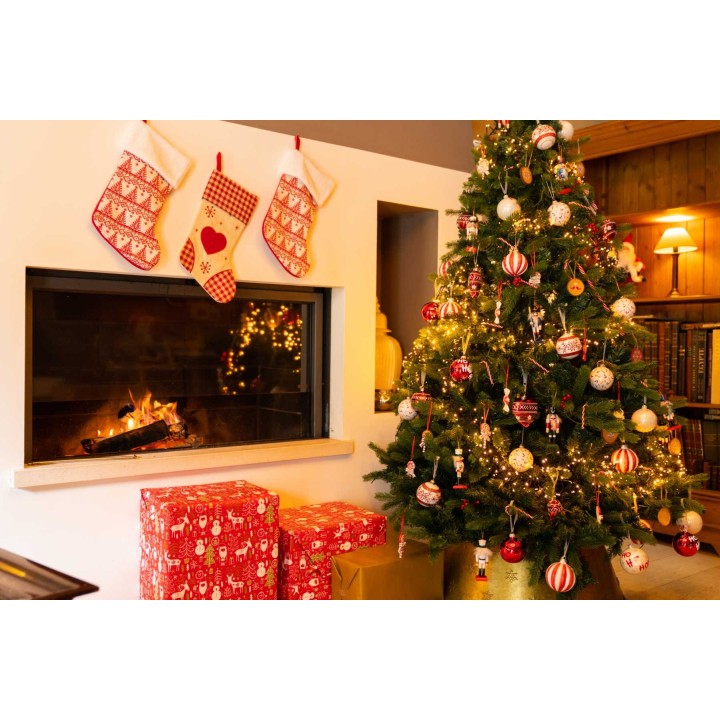 Kerstboom met versieringen, warme kleuren, geschenken en een knisperend haardvuur.