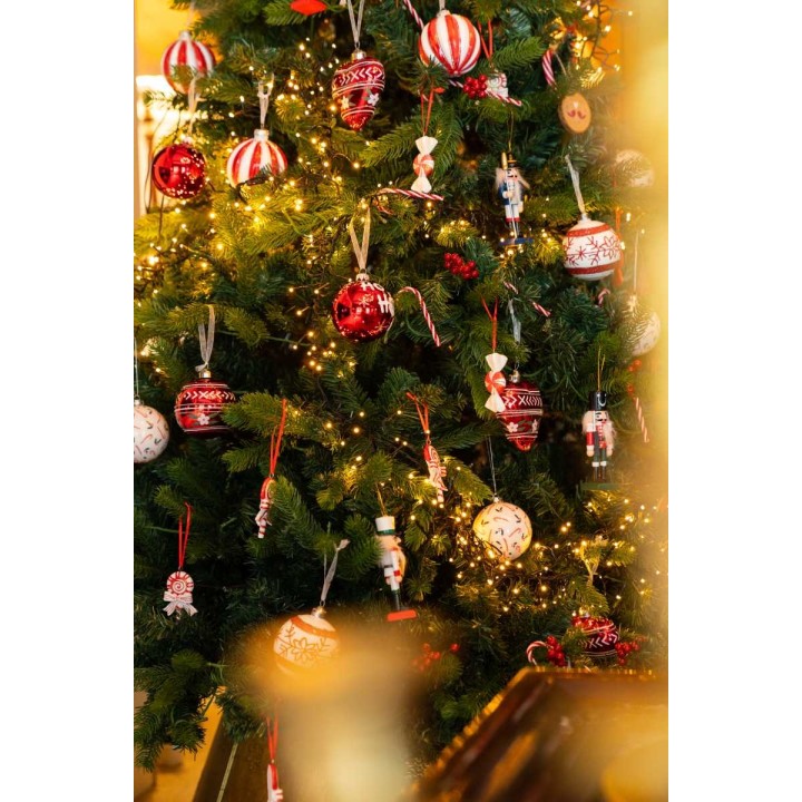 Een feestelijke kerstboom versierd met rode en witte ballen, lichtjes en vrolijke ornamenten.