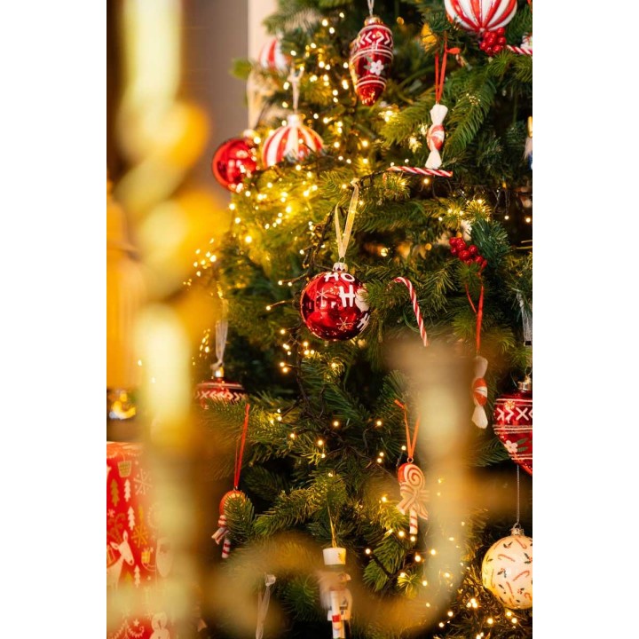 Kerstboom vol kleurrijke ballen, snoepjes en twinkelende lichtjes in een feestelijke sfeer.