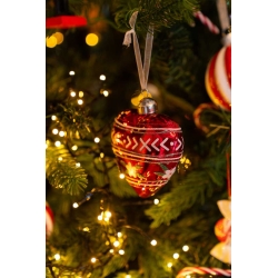 A shiny red ornament with white patterns hangs amid twinkling lights on a festive tree.