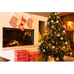 Kerstboom met rode decoraties, cadeaus en een open haard, sfeervol verlicht in warme kleuren.