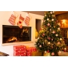 Kerstboom met rode decoraties, cadeaus en een open haard, sfeervol verlicht in warme kleuren.
