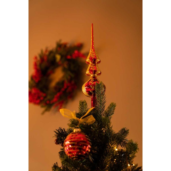 Een kerstboomtopper in goud met een rode kerstbal, op de achtergrond een groene krans.