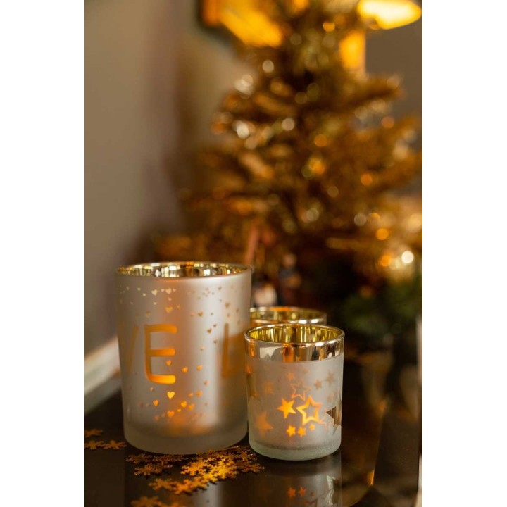 Drie glazen kaarsenhouders met gouden accent, omgeven door een feestelijke sfeer en decoraties.