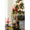 Elegante kaarsenhouder met rode kaarsen, naast een kerstboom en sfeervolle decoraties.