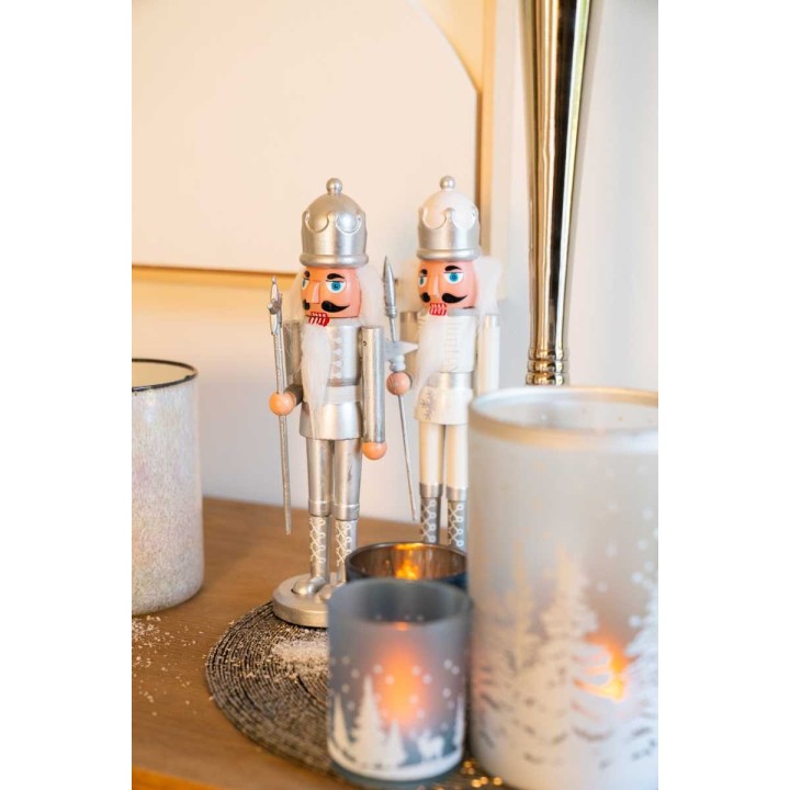 Twee houten kerstfigurines in zilver en wit, omringd door sfeervolle kaarsen en glitters.
