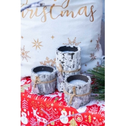 Drie kaarsenhouders van schors, omringd door een feestelijke rode tafelkleed met kerstmotieven.