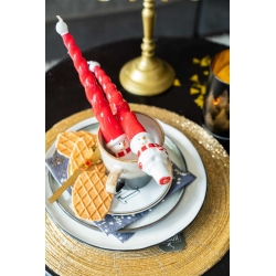 A festive table setting with red twisted candles, a white cup, and waffles on a gold plate.