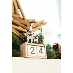 A wooden block calendar with a nature scene of trees and deer, decorated with pine garlands.