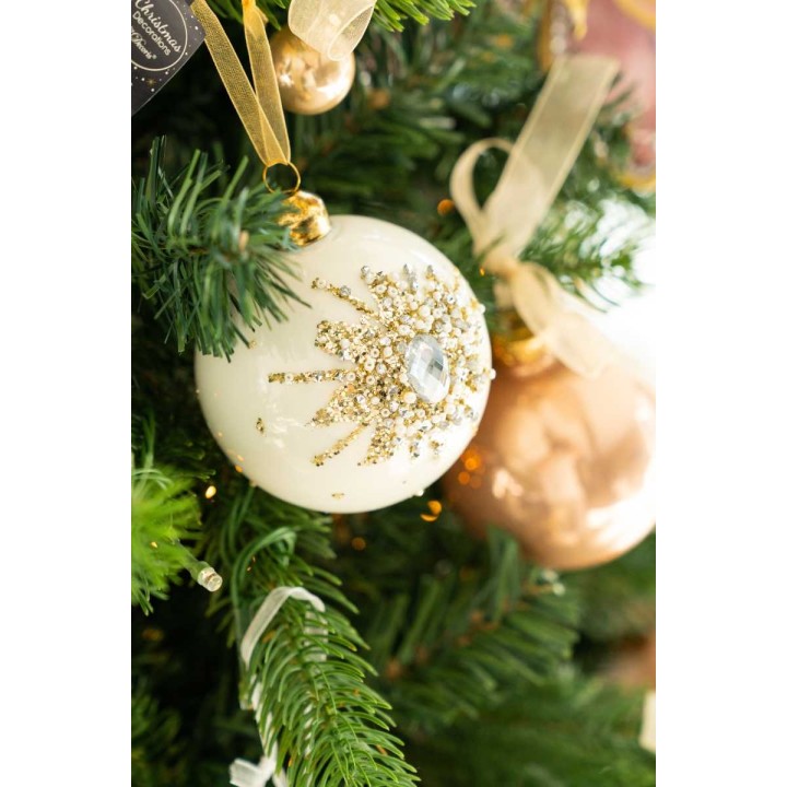 Witte kerstbal met glinsterende gouden versiering hangt tussen groene takken.
