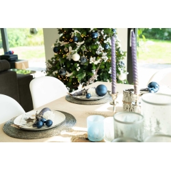 Elegante tafelsetting met blauwe accenten, kerstboom op de achtergrond en sfeervolle kaarsen.