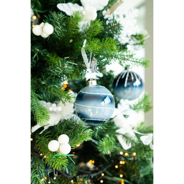 Een groene kerstboom versierd met blauw-witte ballen en witte takjes.