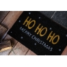 A festive black doormat with "HO HO HO" and "MERRY CHRISTMAS" in cheerful colors.
