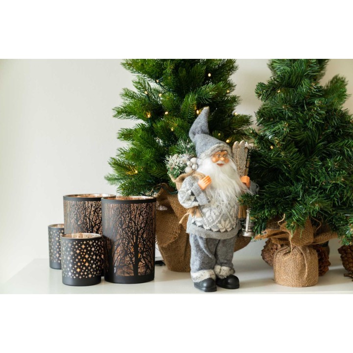 Een kerstmanfiguur naast groene bomen en sfeervolle kaarsenhouders met boommotieven.