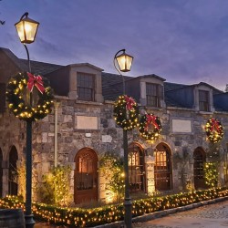 Charming stone buildings adorned with festive wreaths and warm, glowing lights under a twilight sky.