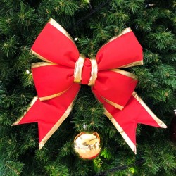 A large, vibrant red bow with gold trim adorns a lush green Christmas tree.