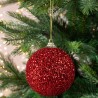 A shiny red glitter ornament hangs from a green evergreen tree.