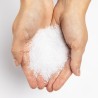 Two hands hold a mound of white, granular salt against a plain background.