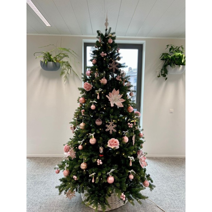 Groene kerstboom versierd met roze ballen, bloemen en sneeuwvlokken, in een lichte ruimte.