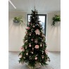 A festive Christmas tree adorned with pink ornaments and flowers, set in a modern room.