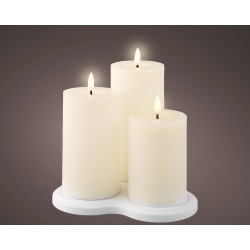 Three glowing white candles of varying heights on a smooth, round white base.