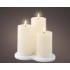 Three glowing white candles of varying heights on a smooth, round white base.