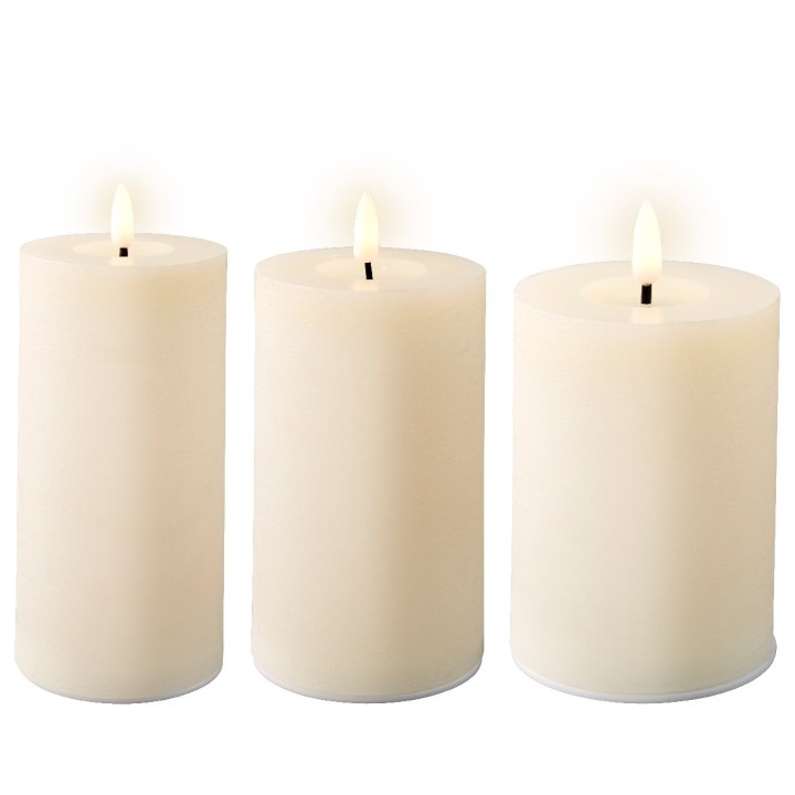 Drie witte kaarsen met een zachte gloed, rechtopstaand op een lichte achtergrond.