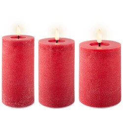 Drie rode kaarsen met een warme vlam, van verschillende hoogtes, op een lichte achtergrond.