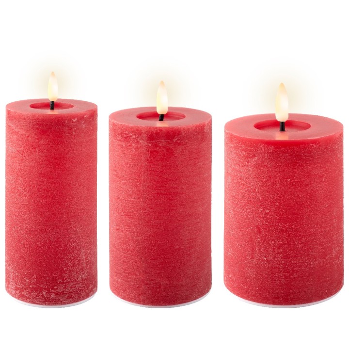 Drie rode kaarsen met een warme vlam, van verschillende hoogtes, op een lichte achtergrond.
