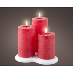Three red pillar candles with soft flames, arranged on a white base against a dark background.