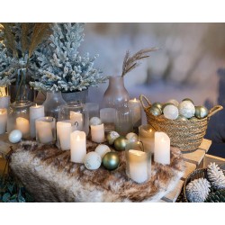 Sfeervolle kerstdecoratie met kaarsen, glazen vazen en groene ornamenten op een zachte ondergrond.