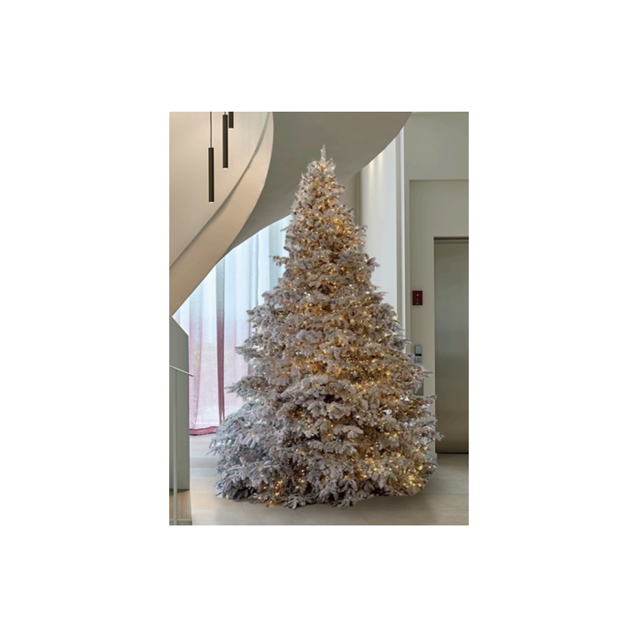 Sneeuwachtige kerstboom met warme verlichting, elegant geplaatst in een moderne interieur.